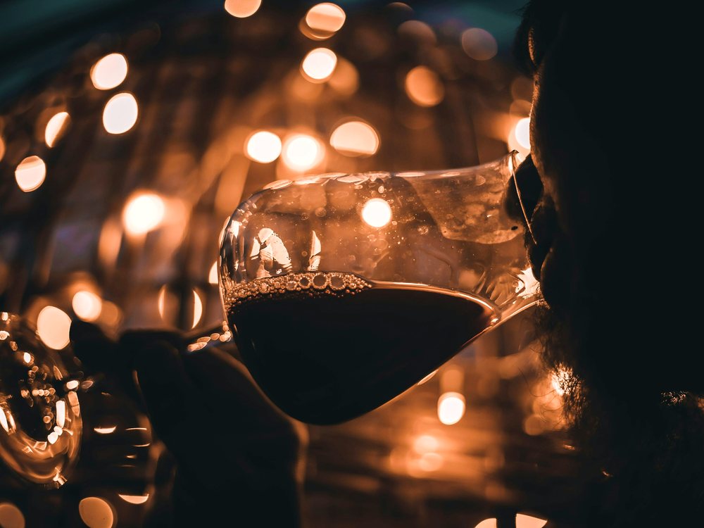 A glass of red wine being poured among candlelight